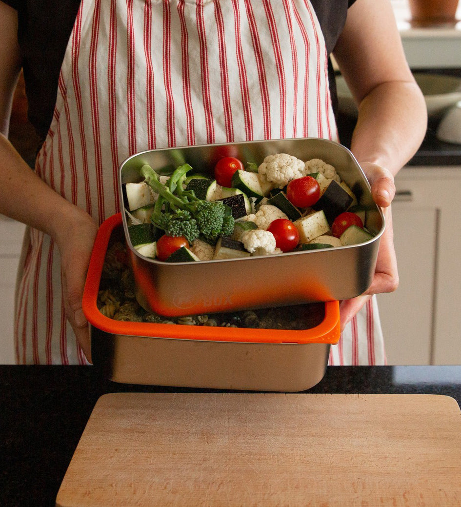 A man holding the Elephant Box Prep & Store large food storage container with an orange silicone seal and see through glass lid.