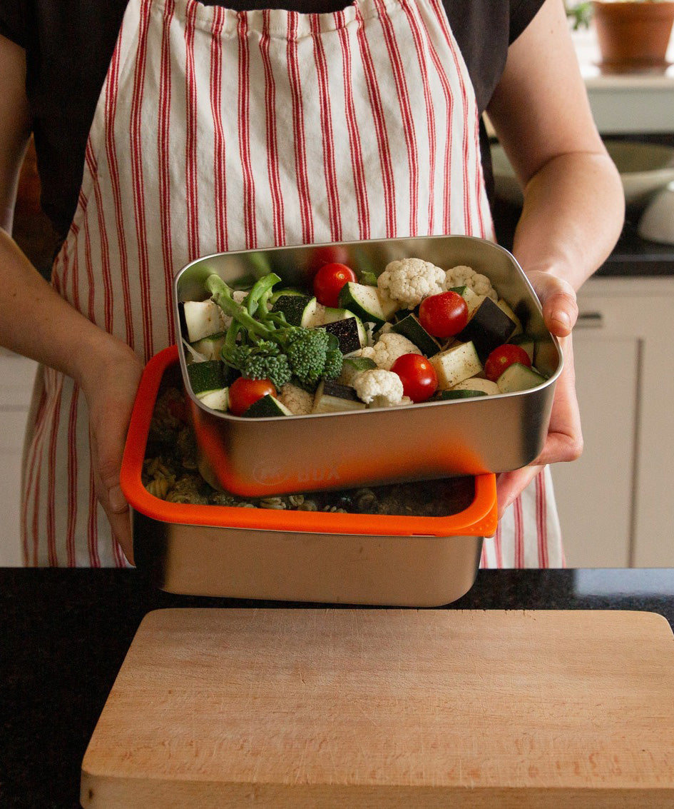 A man holding the Elephant Box Prep & Store large food storage container with an orange silicone seal and see through glass lid.