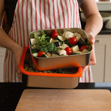 A man holding the Elephant Box Prep & Store large food storage container with an orange silicone seal and see through glass lid.