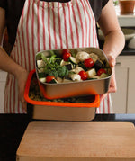 A man holding the Elephant Box Prep & Store large food storage container with an orange silicone seal and see through glass lid.