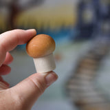 A small white button mushroom with brown shading on the top from the Erzi Forest mushrooms in a box set held up in an adult's hand.