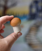 A small white button mushroom with brown shading on the top from the Erzi Forest mushrooms in a box set held up in an adult's hand.