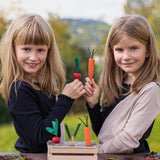 Two children playing with the Erzi Vegetable Patch Wooden Play Food Set. The child on the left is holding the red radish