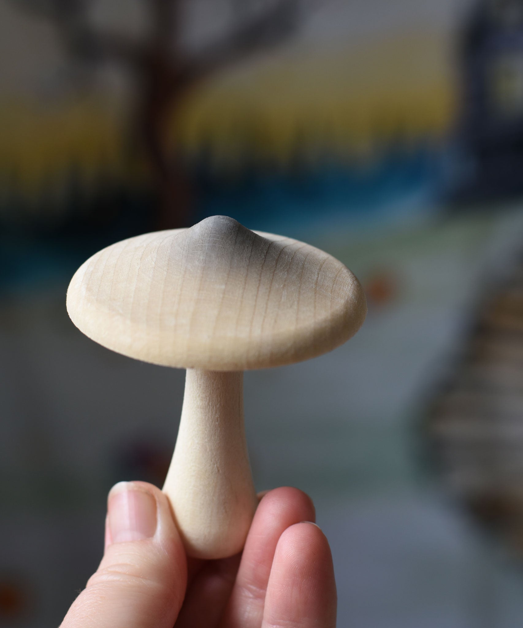 A white coloured mushroom with grey shading on the top from the Erzi Forest mushrooms in a box set held up in an adult's hand.