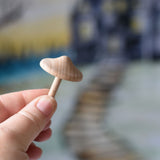 A small wooden mushroom with thin stalk from the Erzi Forest mushrooms in a box set held up in an adult's hand.