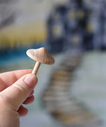 A small wooden mushroom with thin stalk from the Erzi Forest mushrooms in a box set held up in an adult's hand.