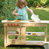 A little girl playing pretend with the Erzi outdoor wooden play kitchen on a sunny day.