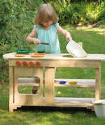 A little girl playing pretend with the Erzi outdoor wooden play kitchen on a sunny day.