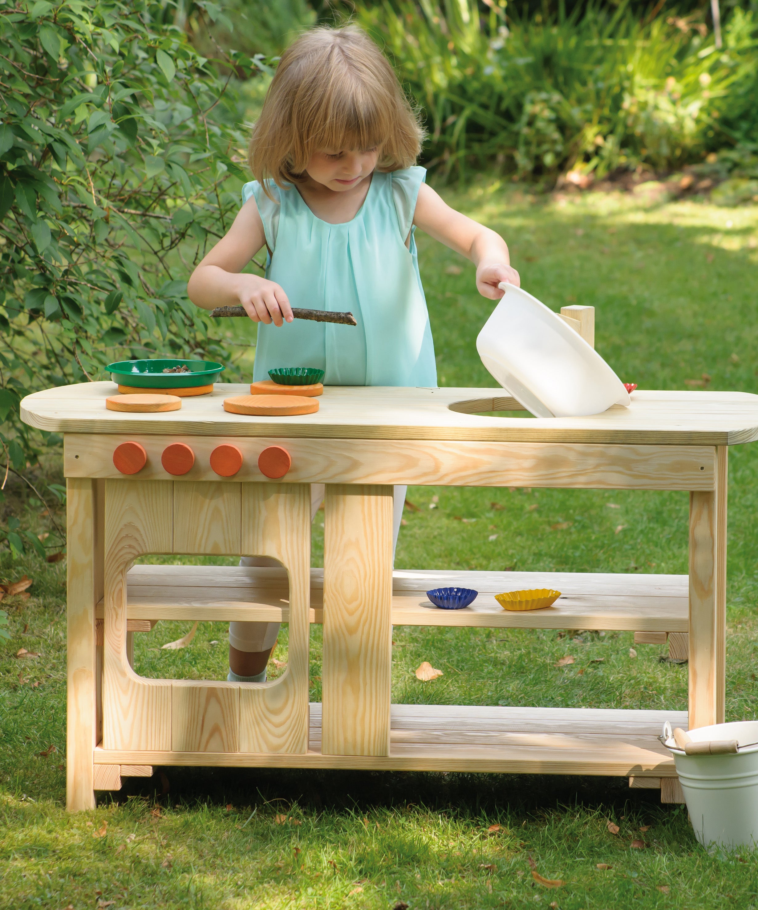 A little girl playing pretend with the Erzi outdoor wooden play kitchen on a sunny day.