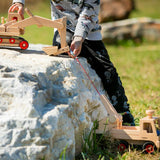 Child playing with the Fagus handmade wooden truck and excavator toy on a large white rock