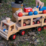 Close up of childs hand holding the Fagus large wooden car transporter lorry toy on some wet grass and autumn leaves