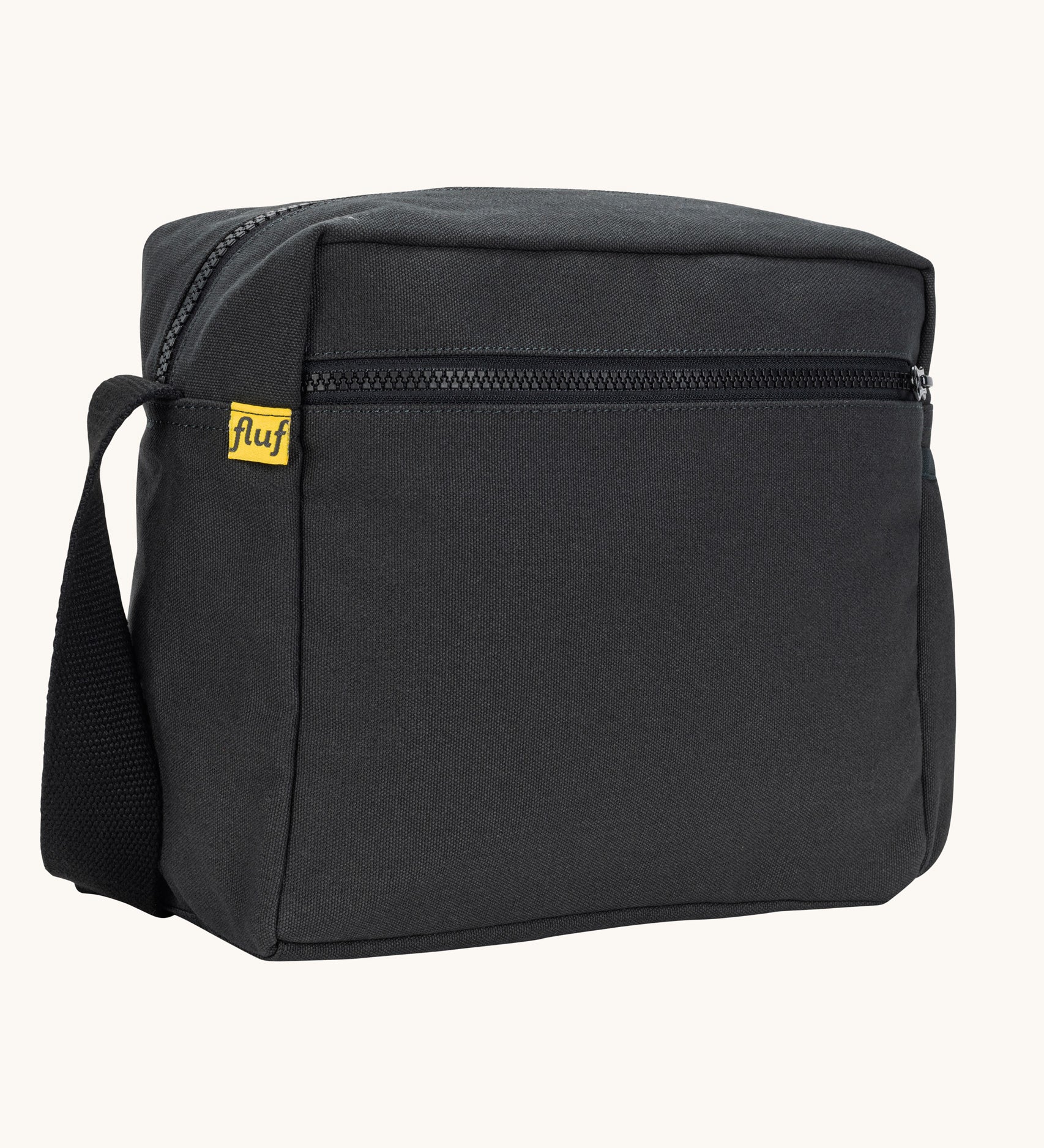 A side angle view of the black carbon coloured Fluf Crossbody Bag. The bag has a black coloured zip and crossbody strap.