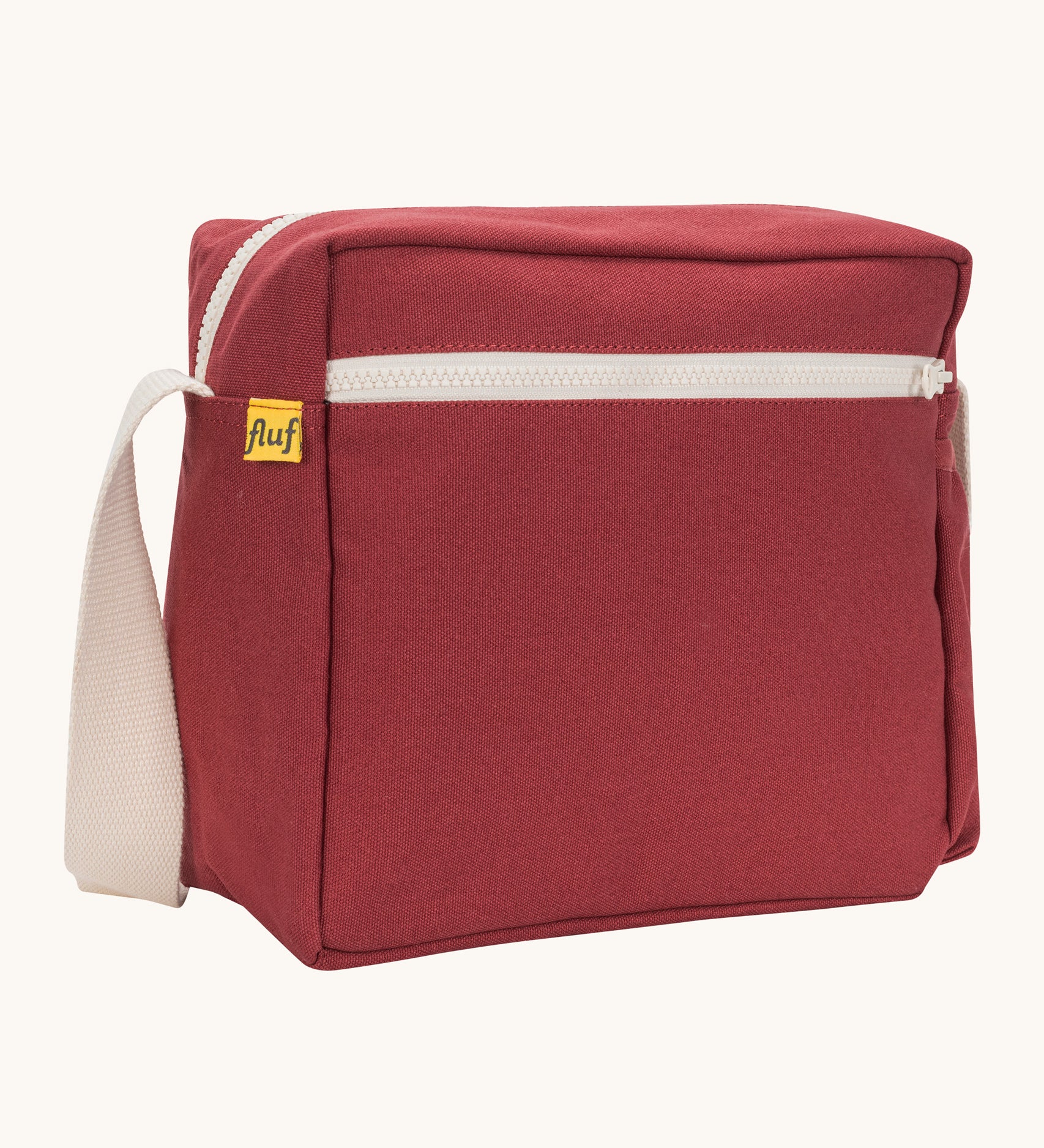 A side angle view of the vintage burgundy coloured Fluf Crossbody Bag. The bag has and off white coloured zip an crossbody strap.