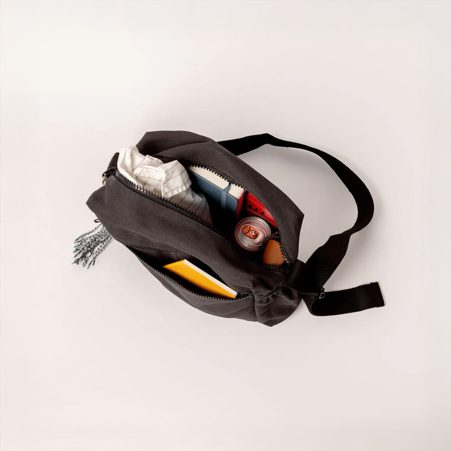 A top view of the Fluf organic cotton crossbody bag with sectioned pockets, showing items that fit inside