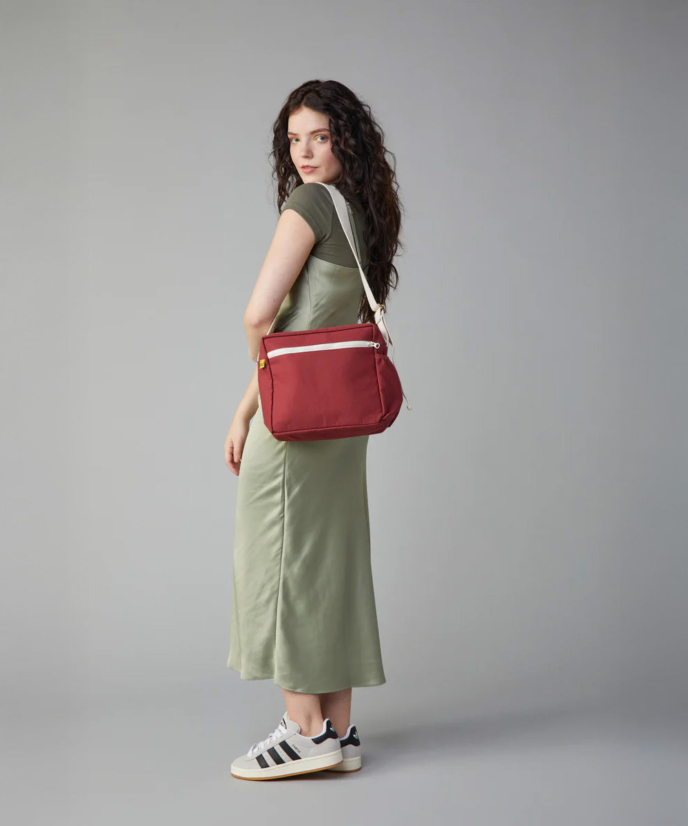 A woman in a green dress modelling the Fluf organic cotton crossbody lunch and every day bag in vintage burgundy