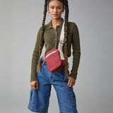 A woman with braided hair, wearing the burgundy organic cotton Mini Crossbody bag from Fluf, a sporty and sleek bag for snacks, travel, and festivals