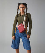 A woman with braided hair, wearing the burgundy organic cotton Mini Crossbody bag from Fluf, a sporty and sleek bag for snacks, travel, and festivals