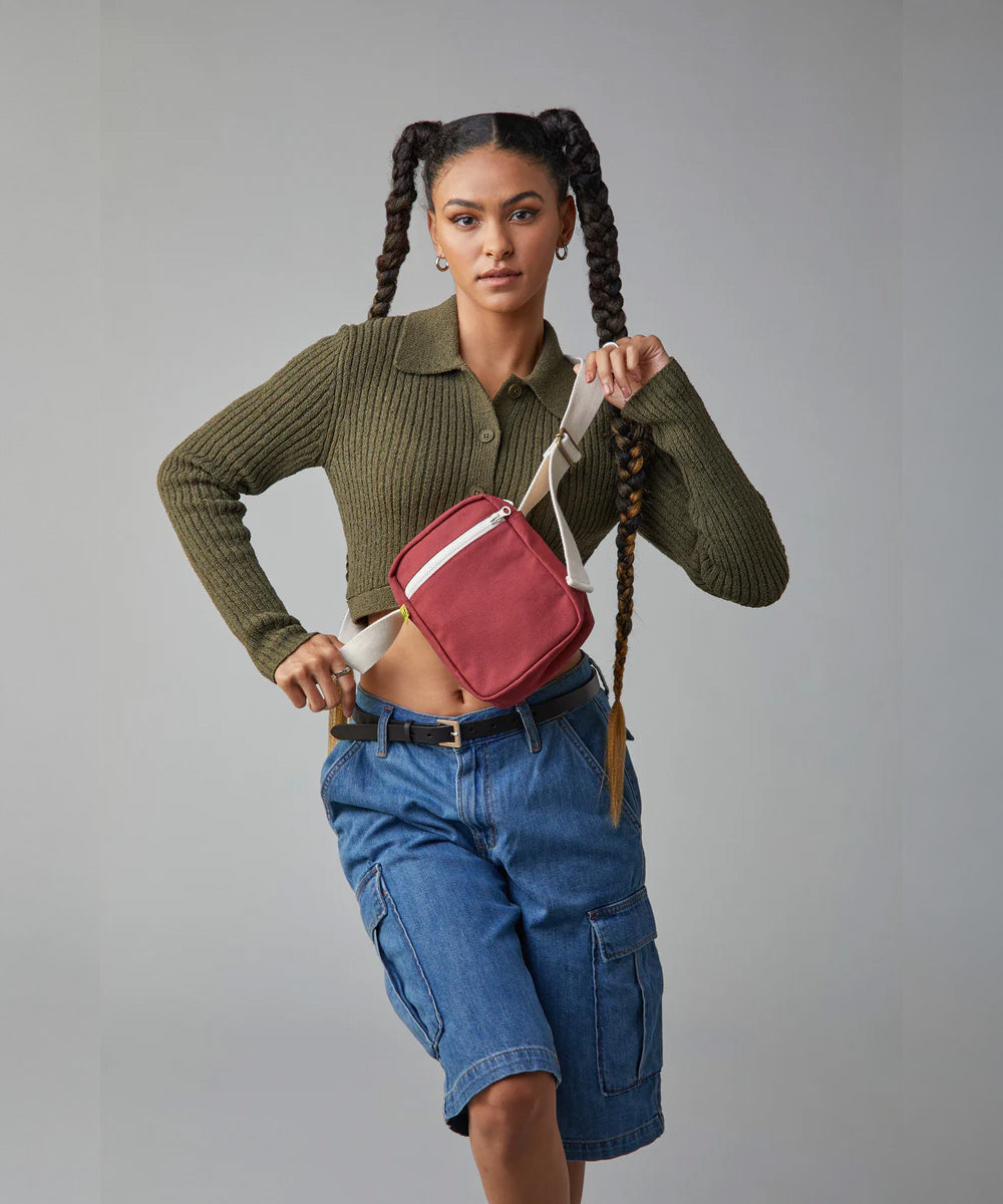 A woman with braided hair modelling the Fluf organic cotton mini crossbody bag, in vintage burgundy.