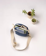 A top view of the Fluf organic cotton mini crossbody bag in navy, holding an iPhone and small notebook in the separated lined pockets.