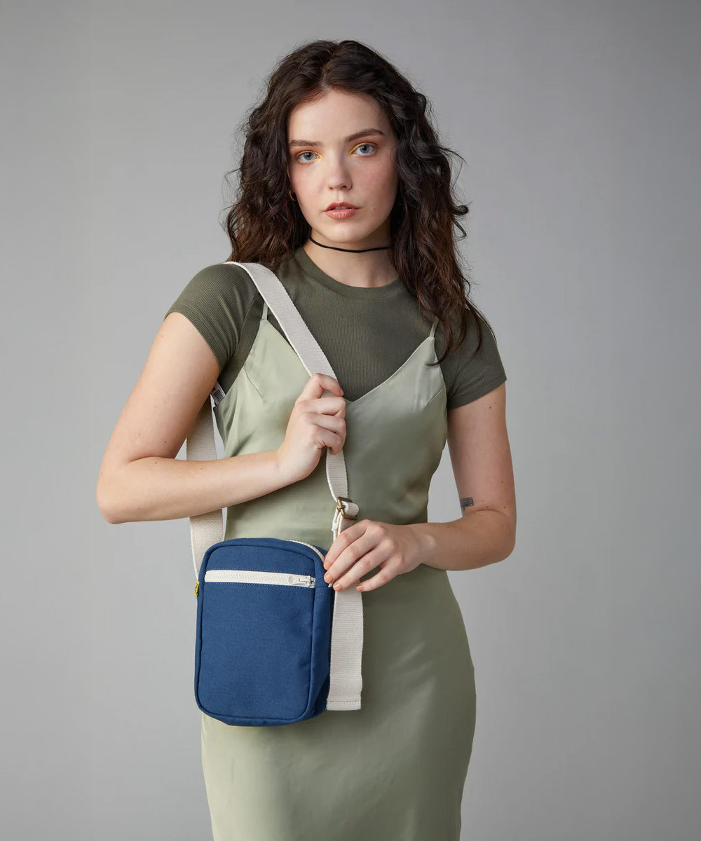 A woman in a green dress wearing the Fluf organic cotton mini crossbody travel organiser and snack bag in navy blue