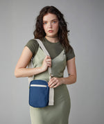 A woman in a green dress wearing the Fluf organic cotton mini crossbody travel organiser and snack bag in navy blue