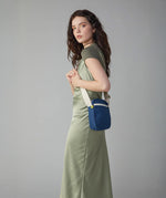 A woman in a green dress wearing the Fluf organic cotton mini crossbody travel organiser and snack bag in navy blue