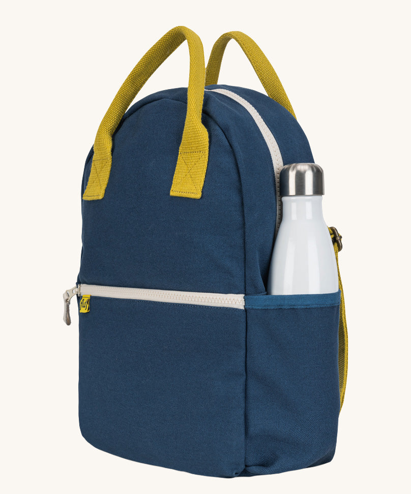 The organic cotton kids Fluf B-Pack Jr in navy blue, the backpack is zipped up and there's a reusable water bottle in the side pocket.