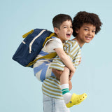 A child wearing a navy coloured Fluf junior backpack whilst having a piggy back from an older child. Both are smiling.