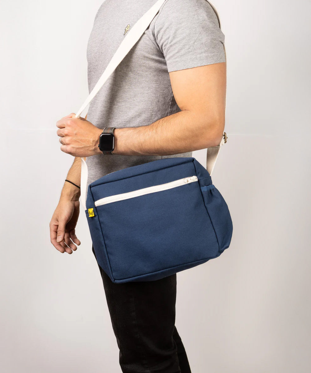 A side view of a man's torso, who's carrying the Fluf organic cotton everyday lunch crossbody bag in navy blue with a white strap.