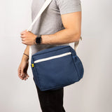 A side view of a man's torso, who's carrying the Fluf organic cotton everyday lunch crossbody bag in navy blue with a white strap.