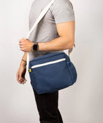A side view of a man's torso, who's carrying the Fluf organic cotton everyday lunch crossbody bag in navy blue with a white strap.