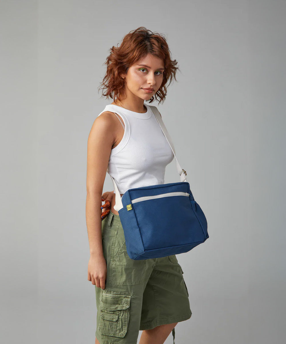A woman wearing the organic cotton Fluf crossbody bag in navy blue with a white adjustable strap.