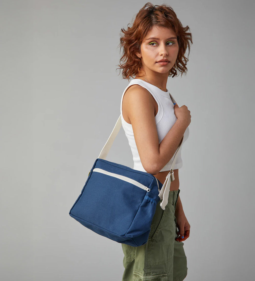 The side profile of a woman carrying the Fluf organic cotton crossbody lunch bag in navy blue over her shoulder.