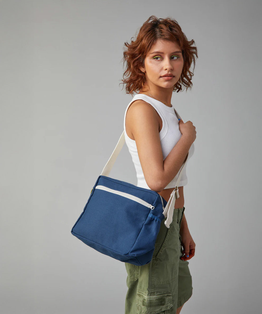 The side profile of a woman carrying the Fluf organic cotton crossbody lunch bag in navy blue over her shoulder.