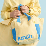 A close up of a person holding the Fluf organic cotton zippered lunch bag in a light butter yellow colour.