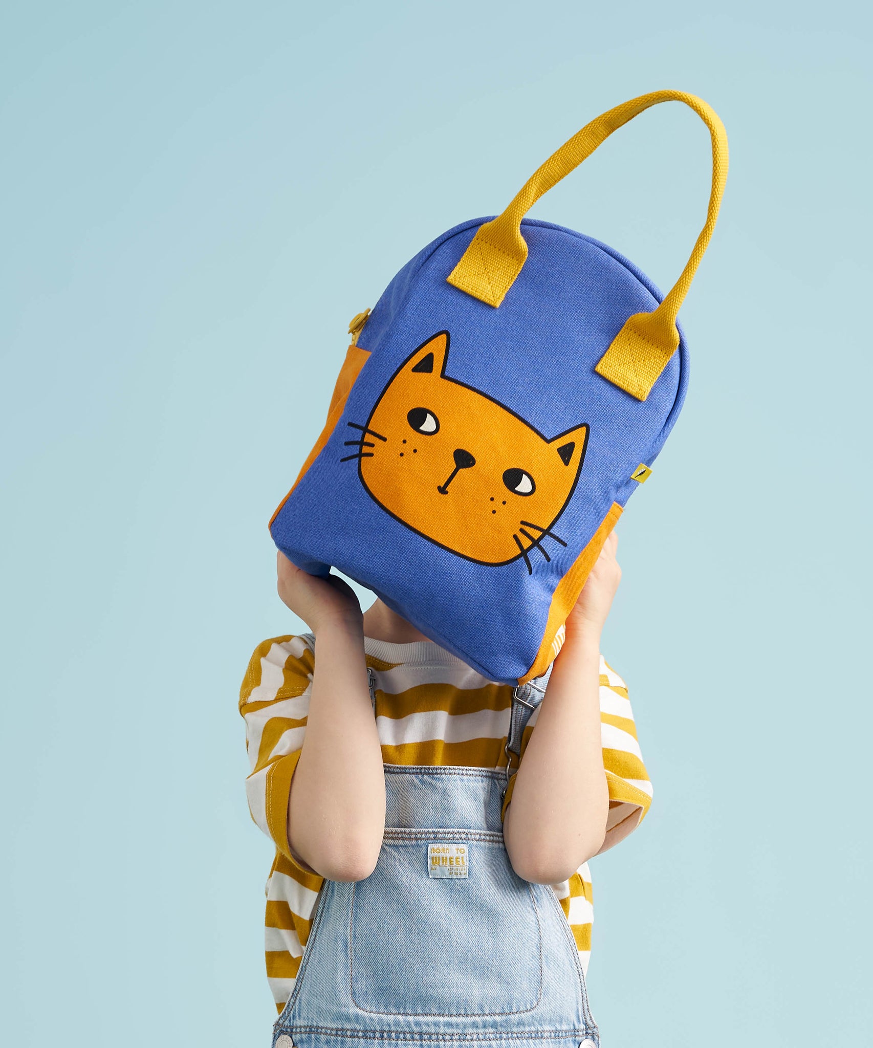 A child holding up the Fluf organic cotton zippered lunch bag, featuring a cat design .