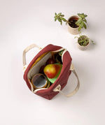 A top view of the Fluf organic cotton zippered lunch bag in a vintage burgundy colour, filled with food containers, fruit, and a water bottle.