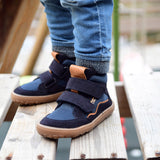 A close up of a child wearing the Froddo barefoot Tex Autumn children's shoe in dark blue available at Babipur. A children's waterproof shoe with a 2 velcro fastener on the front for a secure fit, padded ankle and a brown grippy sole.