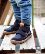 A close up of a child wearing the Froddo barefoot Tex Autumn children's shoe in dark blue available at Babipur. A children's waterproof shoe with a 2 velcro fastener on the front for a secure fit, padded ankle and a brown grippy sole.