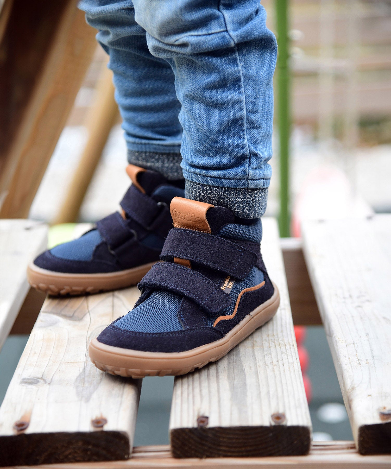 A close up of a child wearing the Froddo barefoot Tex Autumn children's shoe in dark blue available at Babipur. A children's waterproof shoe with a 2 velcro fastener on the front for a secure fit, padded ankle and a brown grippy sole.
