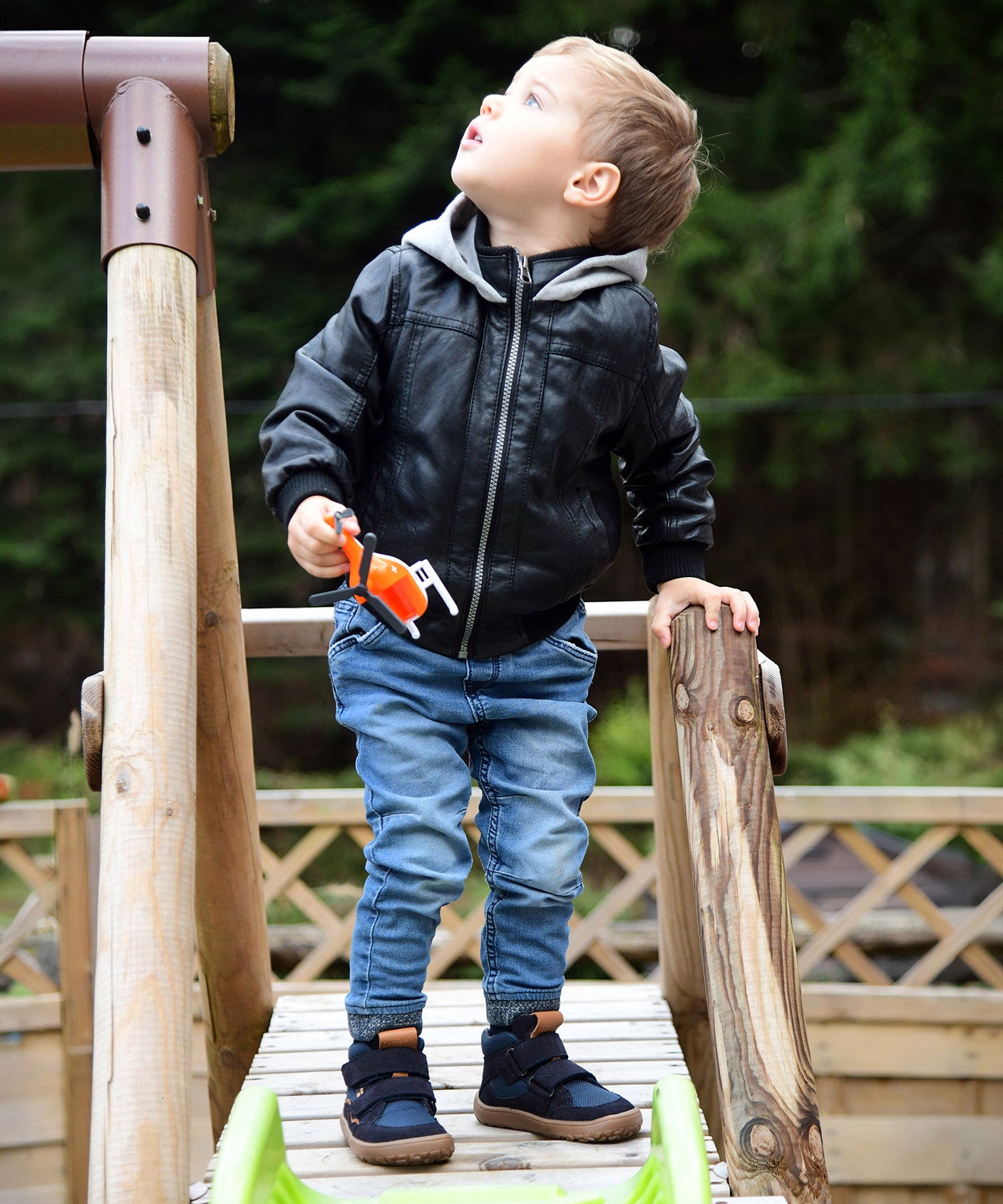 A child playing in the park and wearing the Froddo barefoot Tex Autumn children's shoe in dark blue available at Babipur. A children's waterproof shoe with a 2 velcro fastener on the front for a secure fit, padded ankle and a brown grippy sole.