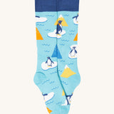 A close up of the Frugi light blue penguin brilliant boot sock showing the penguin print and dark blue cuff detail on organic cotton fabric