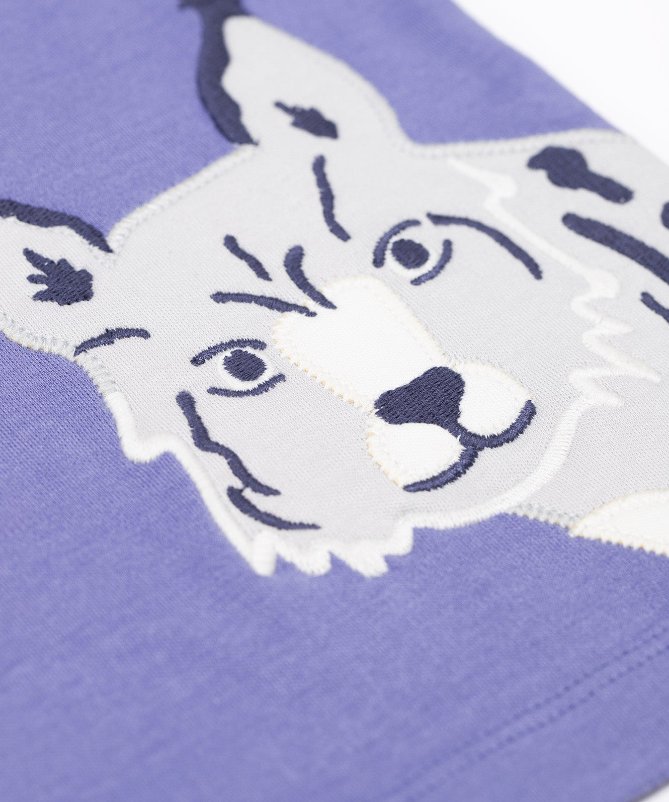 A close up of the snow leopard applique on the Frugi Adventure big cats Applique organic cotton long sleeved top. This top features three big cat appliques on a grape purple coloured background. This top is a part of a wide range of organic cotton clothing for children available here at Babipur.