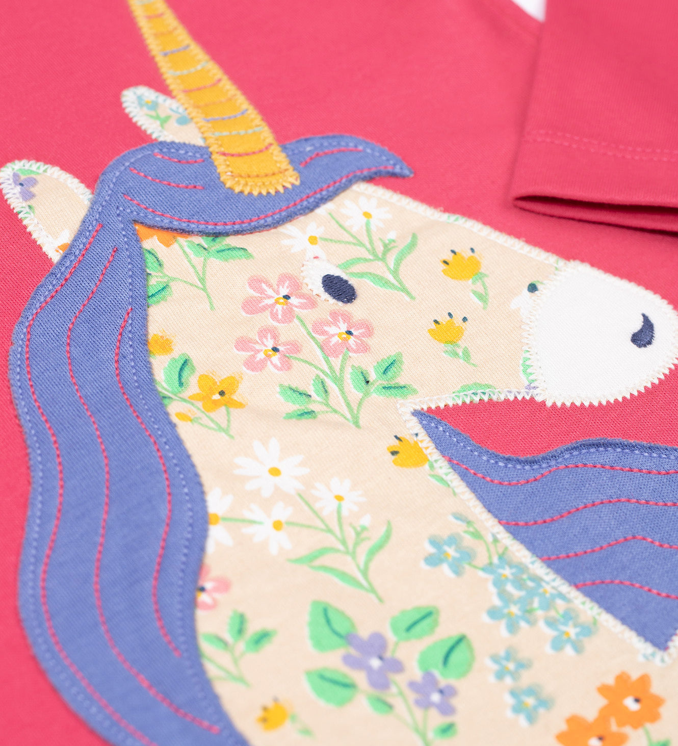 A super close up of teh unicorn applique on the front of the Frugi Rose Pink  Unicorn Anna Circular Organic Cotton Top. A pink coloured long sleeved top with a floral print unicorn applique on the front. This top is a part of a wide range of organic cotton clothing for children available here at Babipur.
