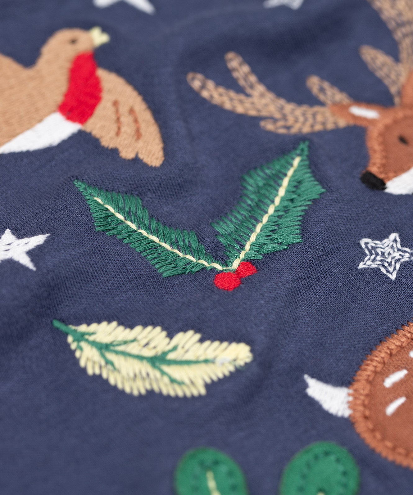 A close up of the embroidered holly detail on the front of the Frugi navy reindeer applique  Organic Cotton Anna long sleeved Top. This top is a part of a wide range of organic cotton clothing for children available here at Babipur.