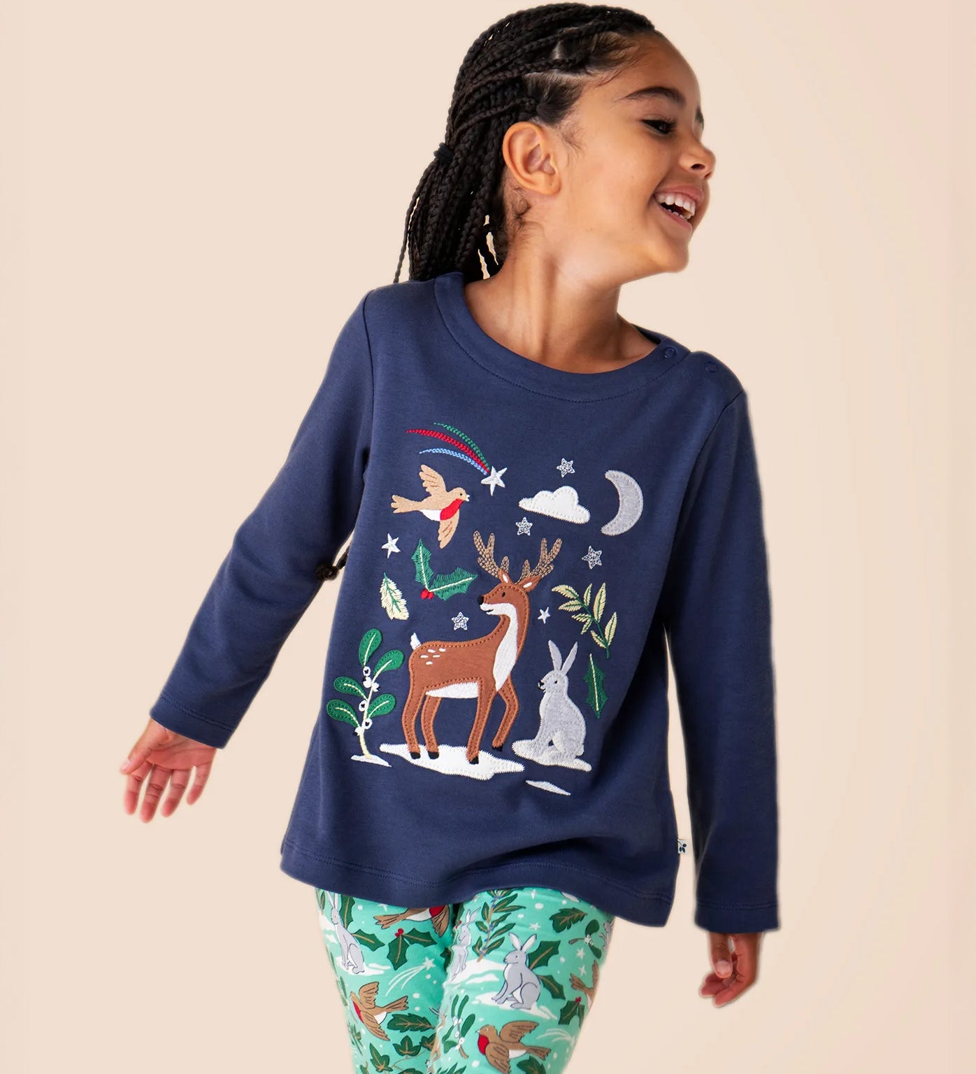 A close up of a child wearing the Frugi navy reindeer Anna top available at Babipur showing the reindeer and woodland animal appliques