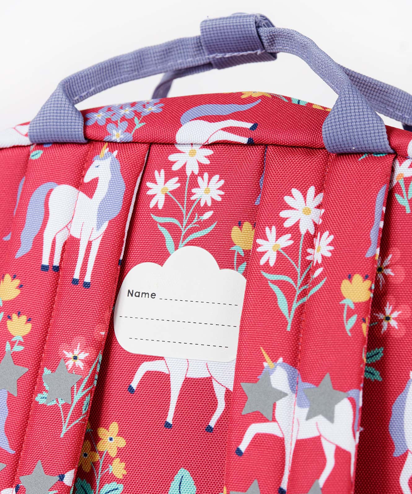 A close up of the back of the Frugi rose unicorn floral explorer backpack showing the name tag patch detail on the top of the bag in between the shoulder straps.