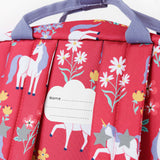 A close up of the back of the Frugi rose unicorn floral explorer backpack showing the name tag patch detail on the top of the bag in between the shoulder straps.
