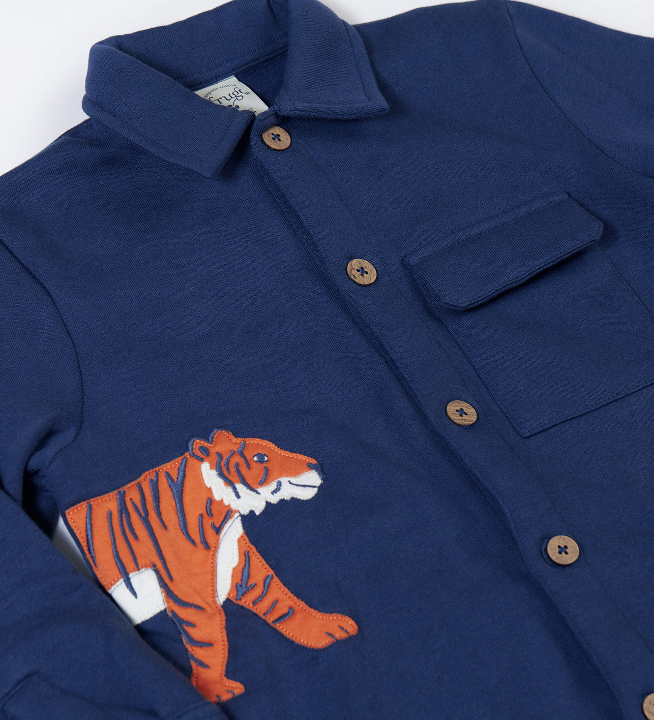 A close up of the orange tiger applique on the side of the Frugi Big Cats Navy Organic Cotton Cosy Kids' Shirt Shaket. This shaket has a tiger and cheetah applique details on the sides. This navy shirt jacket is a part of a wide range of organic cotton clothing for children available here at Babipur.