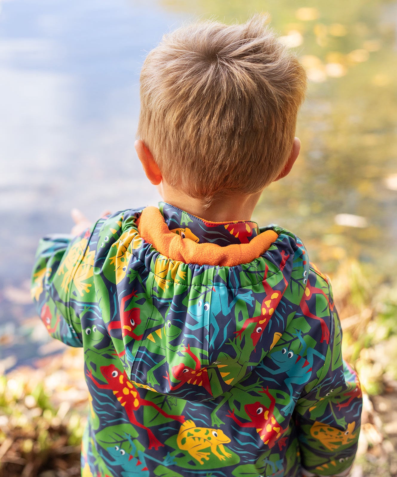 The back of a toddler wearing the Frugi be hoppy puddle buster coat showing the hood detail and orange fleece inside liner.